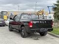 A black 2018 RAM 1500 truck with a crew cab and custom wheels is parked, showcasing its rear design and dual exhaust pipes