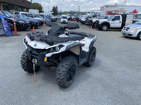 A 2019 Can-Am Outlander all-terrain vehicle with a black and white body design and large knobby tires parked in a lot