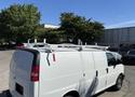 A white 2019 GMC Savana van with a ladder rack on the roof parked in a lot