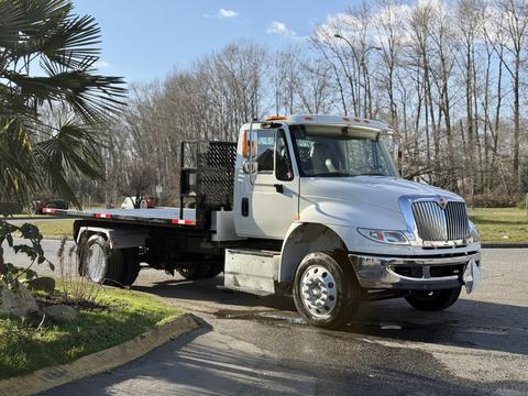 A 2017 International 4300 truck with a flatbed and silver body is parked at an angle showcasing its front and side view