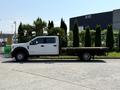 A white 2018 Ford F-550 flatbed truck parked on a paved surface with a flatbed mounted to the chassis