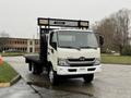 A white 2015 Hino 195 truck with a flatbed and a black rear rack is parked on a street