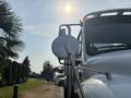 A 2010 Freightliner M2 106 truck with a prominent side mirror reflecting surroundings and a bright sun shining in the sky