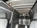 Interior view of a 2025 Mercedes-Benz Sprinter showing two front seats and a spacious cargo area with gray walls and a simple floor design