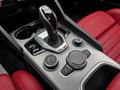 The gear shift and control interface of a 2023 Alfa Romeo Giulia featuring a sleek design with metal and leather accents and red leather seats