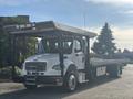 A 2022 Freightliner M2 106 flatbed truck with a white cab and metallic flatbed featuring a protective roof structure