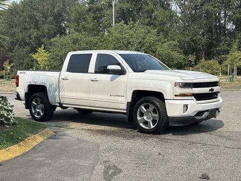 A 2017 Chevrolet Silverado 1500 in white with chrome accents parked on a paved surface featuring a crew cab and large alloy wheels