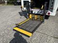A 2018 Ford Transit-350 with a lowered wheelchair ramp featuring a yellow and black color scheme and a mesh surface for accessibility