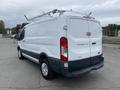 A white 2017 Ford Transit van with a roof rack and silver wheels parked on a paved surface facing slightly to the right