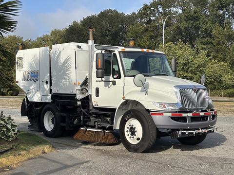 A 2012 International DuraStar 4300 street sweeper with a white body and large brushes on the front for cleaning roads
