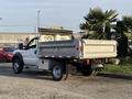 A white 2006 Ford F-550 pickup truck with a dump bed is parked with its bed raised, showcasing its cargo area and rear lighting features