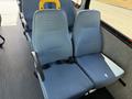 Two light blue upholstered seats with safety belts positioned in a row in a vehicle interior with a yellow handrail adjacent to the seats