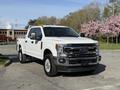 A 2021 Ford F-250 Super Duty pickup truck with a white exterior is parked in view showcasing its front grille headlights and large wheels