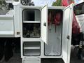 A white truck compartment with two open doors revealing a red hose reel and various equipment components inside
