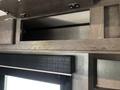 The interior of a 2021 Jayco Jay Flight showing overhead cabinets with a dark wood finish and an empty compartment