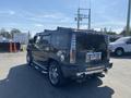 A black 2003 Hummer H2 with chrome accents and dual exhausts parked with its rear view facing the camera