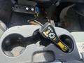 A control panel with buttons and a display sits in the cup holder of a vehicle's center console