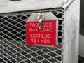 A metal tool box label displaying maximum load capacity of 1000 lbs and 454 kgs attached to a mesh structure