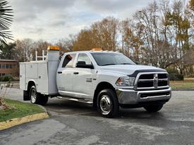 A white 2013 RAM 3500 truck with a utility bed and orange safety lights on top parked on a paved surface