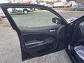 A black 2015 Dodge Charger with an open driver's side door showcasing the interior door panel and controls