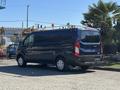 A 2016 Ford Transit 150 van with a blue exterior and roof rack parked with its back facing the viewer