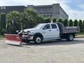 A 2013 RAM 5500 truck with a snow plow attachment on the front and a flatbed in the rear, parked at the forefront of the image