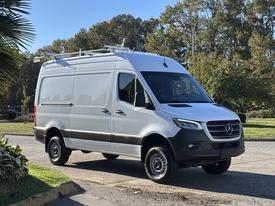 A 2024 Mercedes-Benz Sprinter 2500 van with a sleek design features a white body, black accents, and a roof rack for additional cargo space