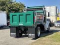 A green 2015 Peterbilt 337 dump truck with a metallic bed and large rear wheels is parked with its dump bed in the upright position