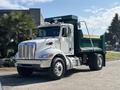 A 2015 Peterbilt 337 dump truck in white and green with a shiny front grille and cab featuring roof lights and a raised dump bed