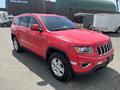 A red 2015 Jeep Grand Cherokee parked on a surface with a clear view of its front and side features including large wheels and a distinctive grille