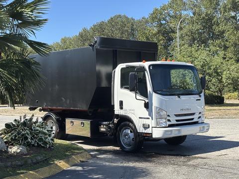 2016 Isuzu NPR-HD truck with a large black cargo box and orange lights on top parked on a street