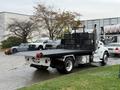 A white 2020 Peterbilt 330 flatbed truck with a black mesh safety cage on the bed and red tow hooks attached to the rear