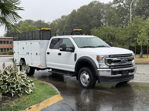 A 2020 Ford F-550 in white with a utility body and yellow lights on the roof parked at an angle with rain falling around it