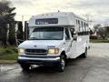 A white 2002 Ford Econoline bus with large windows and a boxy shape parked on a paved surface