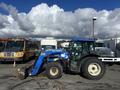 A blue 2010 New Holland T4050 tractor with a front loader attachment parked in a lot with vehicles in the background