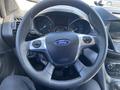 Steering wheel of a 2016 Ford Escape featuring the Ford logo and various controls with a dashboard display in the background