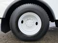 A close-up view of a large black tire with a white wheel rim displaying multiple bolt holes and a patterned tread design