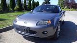 A gray 2007 Mazda Miata with a rounded front and distinctive headlights parked with no license plate visible