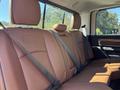 The rear seat of a 2015 RAM 1500 featuring brown leather upholstery and seat belts securely fastened in place