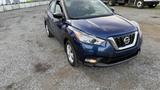 A 2019 Nissan Kicks in blue with a sleek design featuring distinctive headlights and a prominent grille parked on gravel