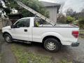 A white 2011 Ford F-150 truck with a ladder rack in the bed and tools visible inside the cabin
