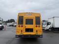 A yellow 2021 Ford Econoline bus viewed from the rear featuring round red tail lights and an open door