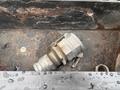 A rusty metal connector resting on a bed of gravel and debris in a compartment of a 2006 Freightliner M2 106