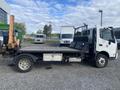 A white 2019 Hino 195 flatbed truck with a black bed visible from the side equipped with a hydraulic lift on the rear