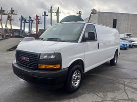 A white 2022 GMC Savana van with a simple front grille design and chrome accents is positioned at an angle showcasing its wheels and side profile
