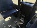 Interior view of a 2020 Chevrolet Express showing two blue seats one is folded up with a tire on the floor and visible hardware components