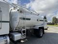 A 2015 Peterbilt 337 truck with a white tanker body featuring a green stripe and a ladder on the side