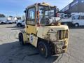 A yellow 1993 Hyster H80XL forklift with an enclosed cab and visible wear and tear on the body features large tires and a hydraulic lift system on the front