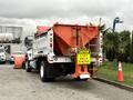 A 2012 International 7400 truck with a large orange salt spreader attached to the back and a caution sign reading "CAUTION STAY BACK 15 METERS" displayed prominently