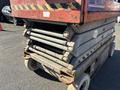 A rusty 2010 SkyJack SJ scissor lift with a red and gray color scheme showing its folded steel support arms and wheels at the bottom